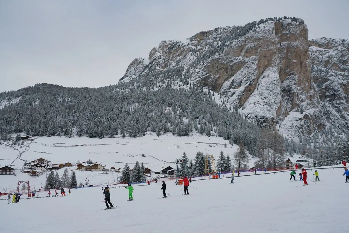 Übungshang mit Skifahrern, dahinter verschneite Felswände