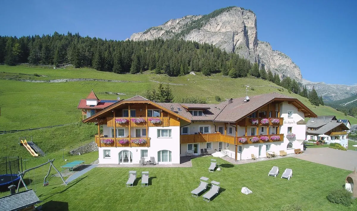 La Majon im Sommer aus der Luft, mit Liegewiese, Spielplatz und Blumenbalkonen