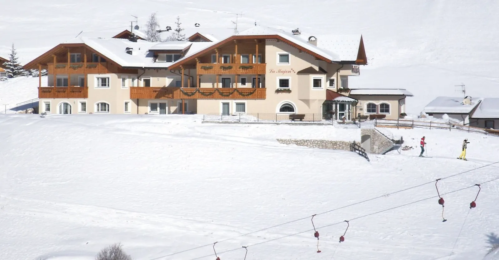 Das Garni La Majon im Schnee, davor der Cadepunt-Lift mit Bügeln und Skifahrer am Übungshang