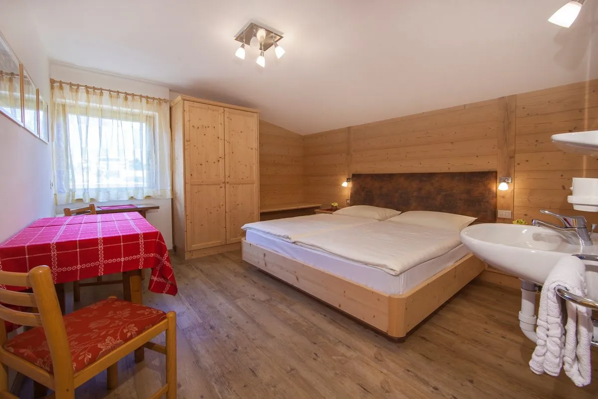 Schlafzimmer im Apartment Puez mit Holzbett und rot kariertem Tisch